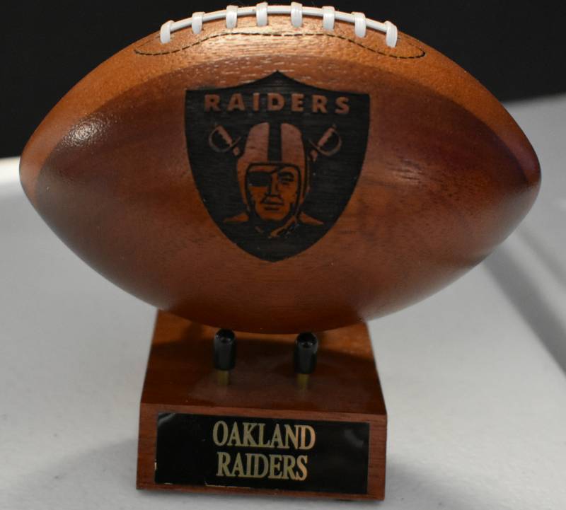 lot 1083 image: Oakland Raiders National Football League Wooden Team Logo Football With Stand - 5 Inches Wide - With Metal Team Name Plaque