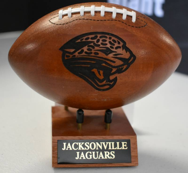 lot 1095 image: Jacksonville Jaguars National Football League Wooden Team Logo Football With Stand - 5 Inches Wide - With Metal Team Name Plaque