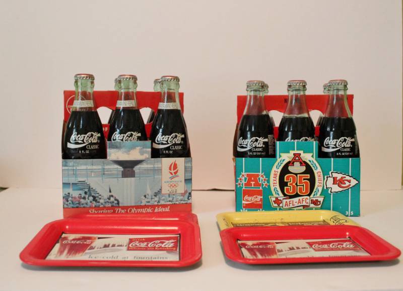 lot 1123 image: Two unopened 6 packs of glass bottled Coke.  One advertising the Olympics and the other the 1994 KC Chiefs AFC - AFL Texans