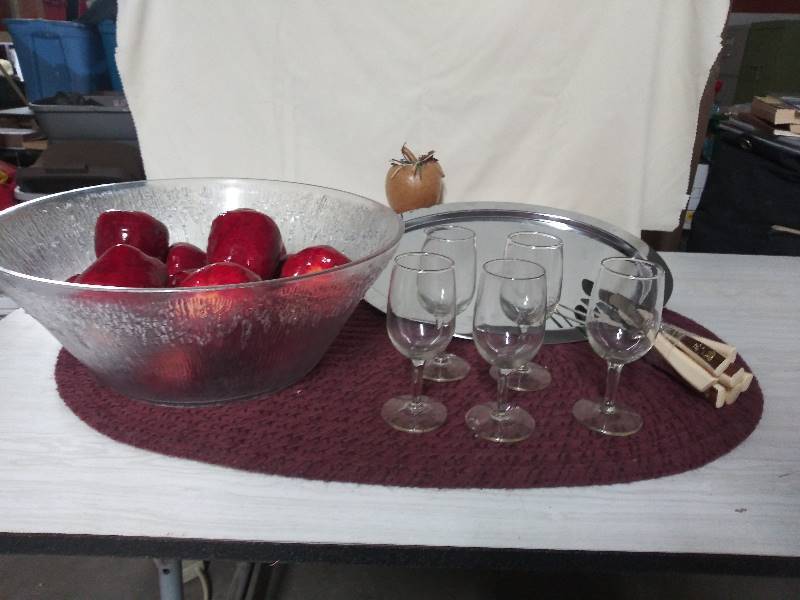lot 2074 image: Five stemmed juice glasses, Silver Platter - not real silver, Large crinkled glass bowl, faux apples, vintage serving silverware that includes serving fork, pie server and serrated knives.
