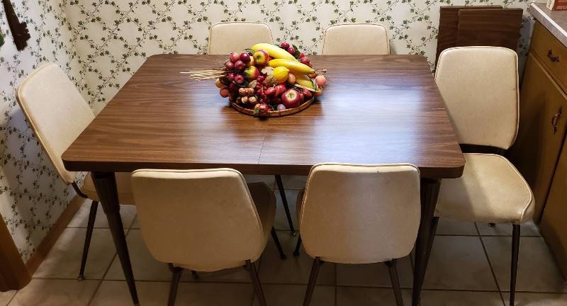 lot 2714 image: Formica Wood Grain Top Table (49 in. x 36 in. plus two 11 in. leaves) and 6 Cream Vinyl Chairs - centerpiece included